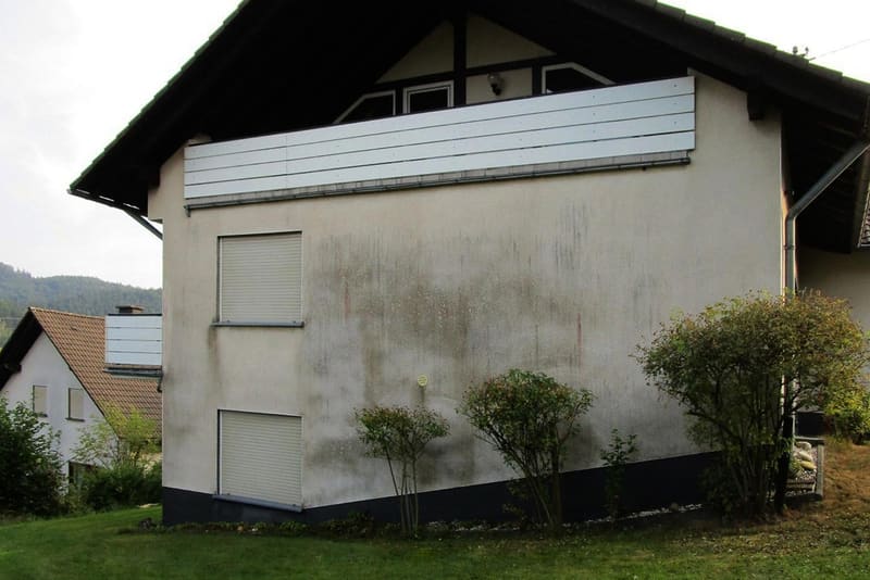 Giebelseite eines Wohnhauses mit dunklen Verfärbungen und Schimmel auf dem hellen Putz, zwei geschlossene Rollläden