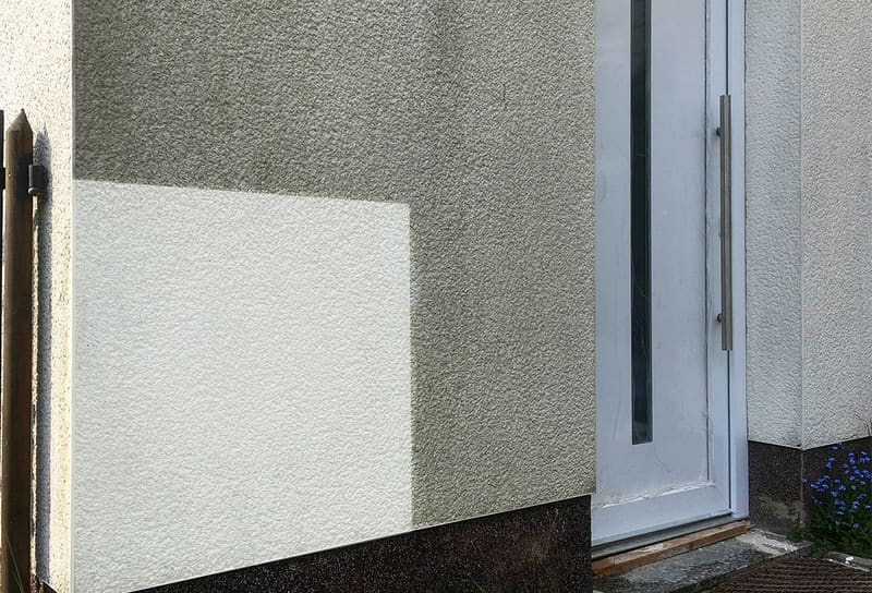 Hell gereinigte, rechteckige Fläche auf einem grau verschmutzten Putz neben einer Haustür