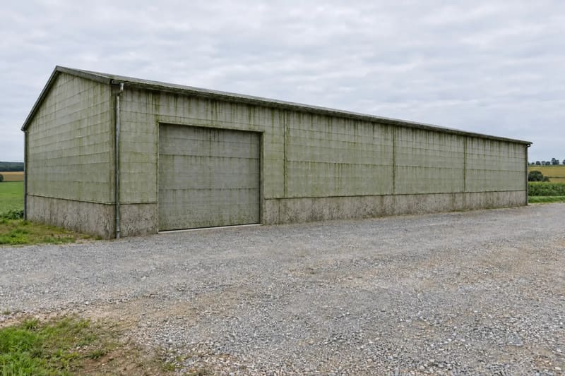 Landwirtschaftliche Maschinenhalle mit Metallfassade, die Außenwand grünlich verschmutzt und fleckig