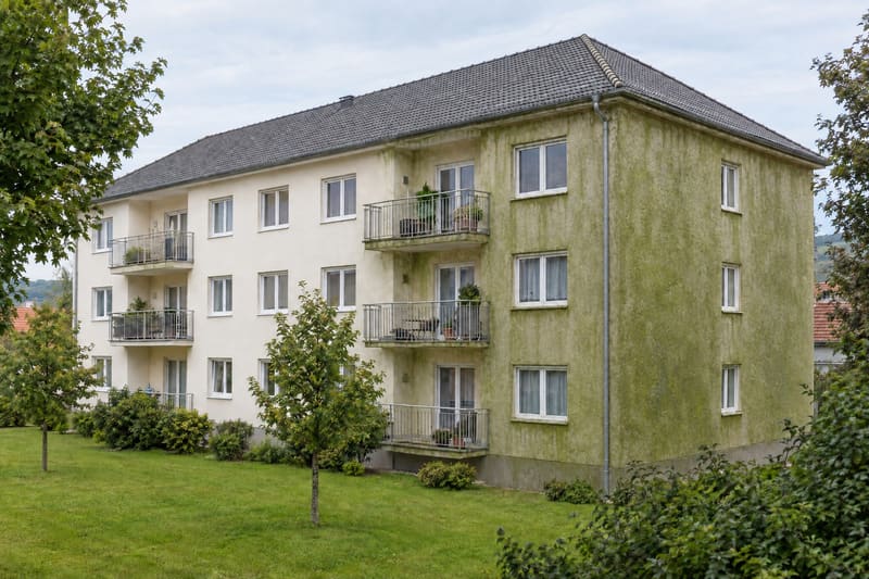 Dreigeschoßige Wohnanlage mit Balkonen, der vorspringende Gebäudeteil und die Giebelwand mit grünem Algenbelag
